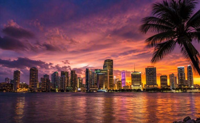 Miami skyline at dusk viewed across Biscayne Bay with glowing city lights reflecting on the water